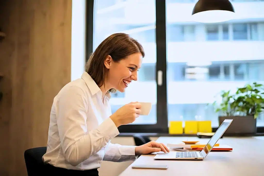 Engenharia de Prompt: Guia Prático Para Usar IA 4 Uma mulher com expressão sorridente e satisfeita, de camisa social branca, trabalhando no notebook, estudando engenharia de prompt, em um escritório iluminado, enquanto segura uma xícara de café.